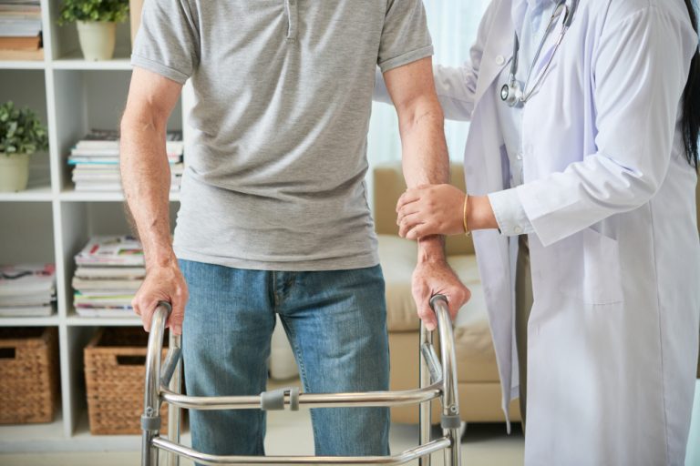 unrecognizable female doctor helping male patient walk with walking frame 1